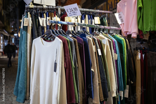 Clothing rack with colorful sweaters at a street market at night.
