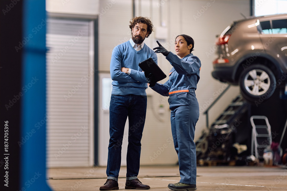 Fototapeta premium Female auto repair shop worker communicating with customer in garage.