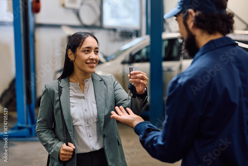 Tableau sur toile Happy woman handing over her car keys to mechanic in workshop.