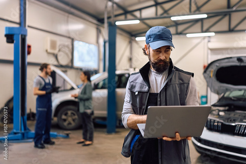 Billede på lærred Mature mechanic working on laptop in auto repair shop.