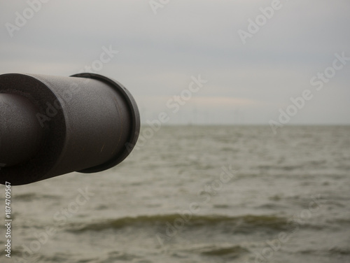 Muzzle of a steel cannon barrel looks out over  gray, endless seeming sea lying in the blurred area. Symbolic image. Represents the necessary willingness to defend ourselves from the distant unknown.