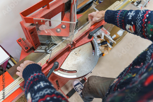 Фотография A craftsman uses a red miter guillotine to cut precise angles on wooden picture frame molding