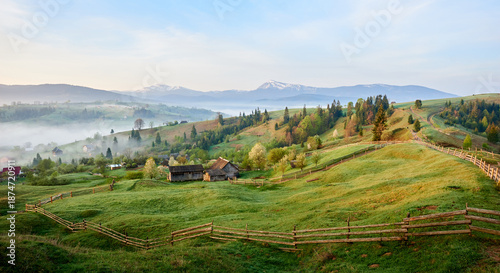 Bilde på lerret Tranquil morning landscape with lush green valley dotted with rustic farm buildings and winding wooden fences