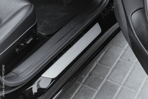 Billede på lærred Close-up of elegant black glossy door sill plate with sleek white illuminated or matte insert in a premium car interior, surrounded by black leather seats and dark carpets