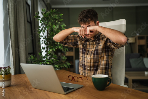 Fotografie Young man rubbing tired eyes at home office desk