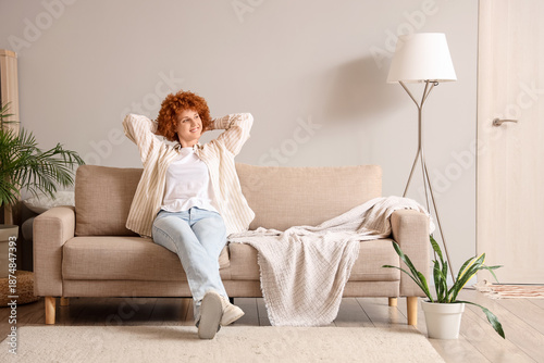 Young redhead woman sitting on sofa at home