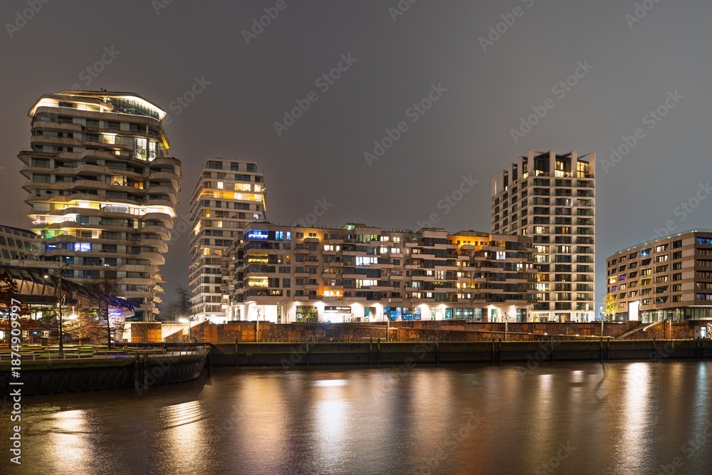 Fototapeta premium Night scene in Hamburg, showcasing modern architecture. Illuminated buildings reflect in the water, capturing the urban vibrancy and design of Hamburg, Germany.