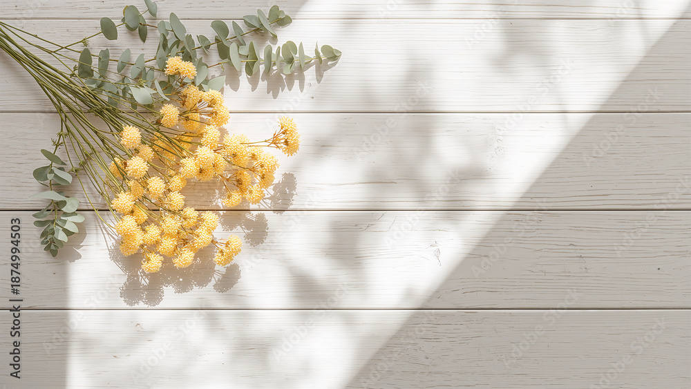 Fototapeta premium 春の午前、窓辺の木製テーブル左上に置いたミモザと木漏れ日の影