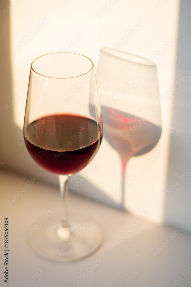 Fototapeta premium A rich glass of red wine sits elegantly, basking in warm sunlight and creating a gentle shadow