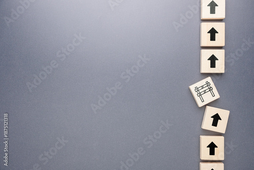 Wooden arrow blocks showing upward progress interrupted by a barrier, representing delay, blockage, and obstacle concept
