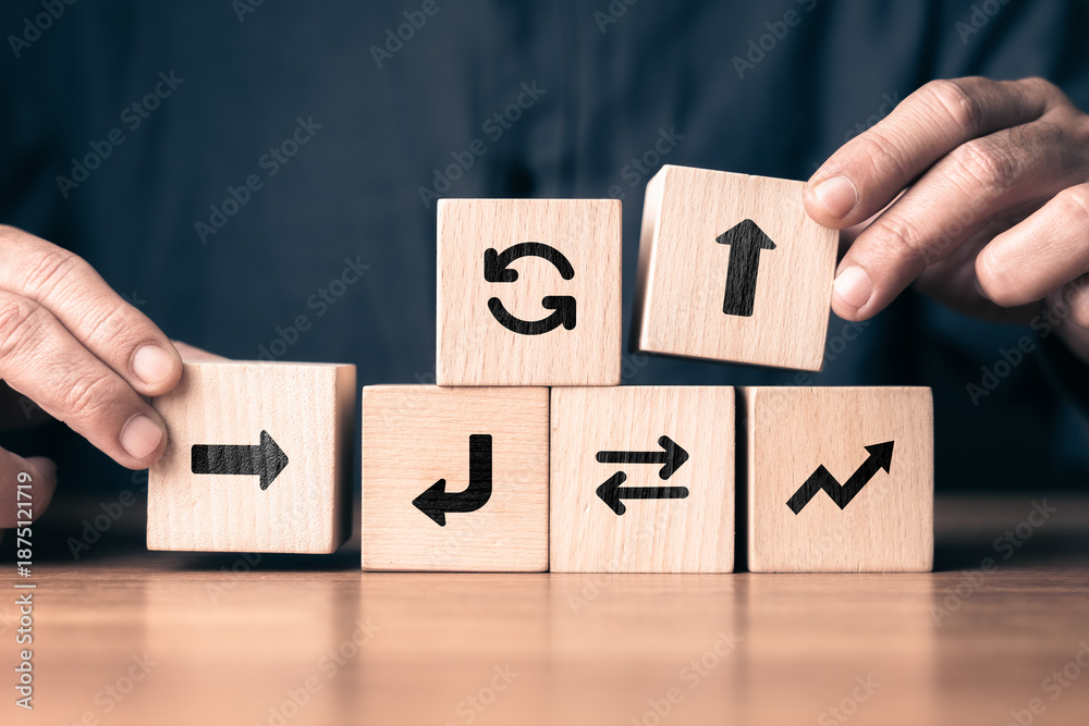 Obraz premium Wooden blocks with arrow symbols arranged by human hands to represent decision making, strategy, and adaptive workflow concept, showing direction changes, planning process