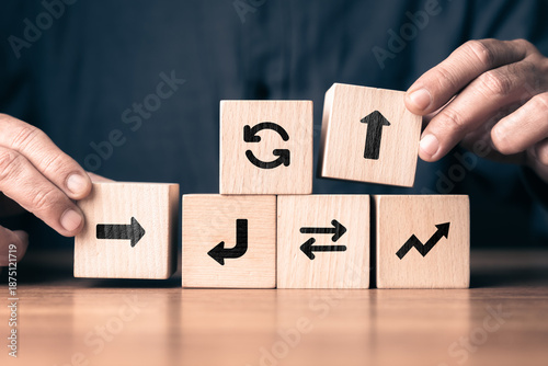 Wooden blocks with arrow symbols arranged by human hands to represent decision making, strategy, and adaptive workflow concept, showing direction changes, planning process © patpitchaya