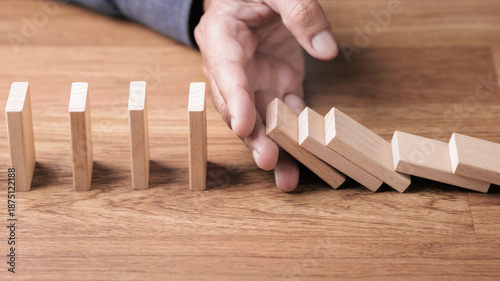 Photos Hand stopping falling wooden blocks like domino to prevent a domino effect, repr