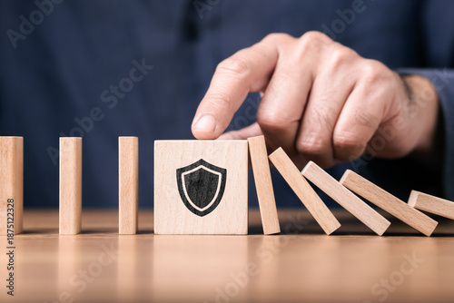 Photography Wooden blocks arranged like domino with a shield symbol blocking the fall, repre