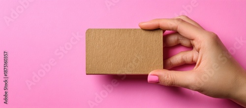 Hand holding a small cardboard box on a pink background.