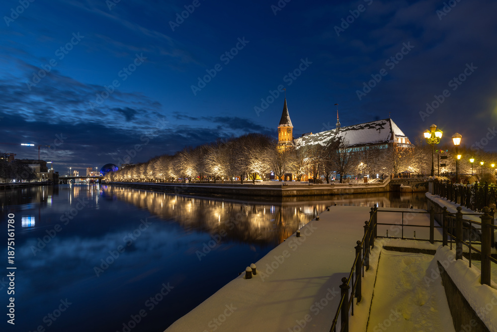 Fototapeta premium The snow-covered embankment of the Fishing Village with Kaliningrad Cathedral in the background, reflected in the river on a winter evening