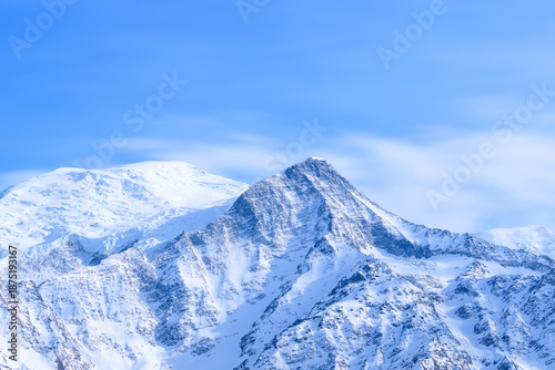 Mont Blanc stands tall with its snow-covered slopes and sharp ridges under a luminous blue sky, showcasing crisp winter textures and serene alpine atmosphere.
