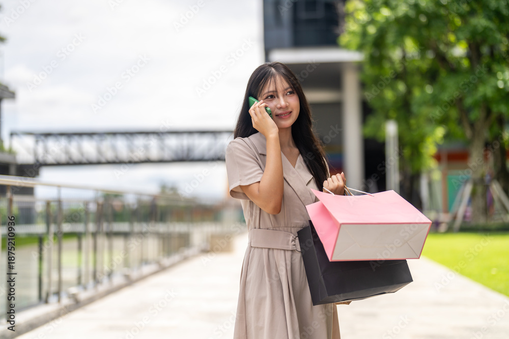 Fototapeta premium Happy asian woman holding shopping bags talking on phone about credit card discount, Girl shopper enjoying end of season sale promotion at department store, Mobile app delivery lifestyle concept
