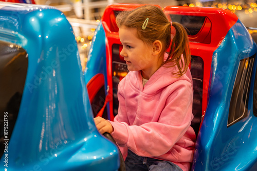 Little girl riding coin operated toy car attraction in shopping mall kids area. Childhood entertainment moment, family leisure activity and everyday fun experience in real life commercial environment