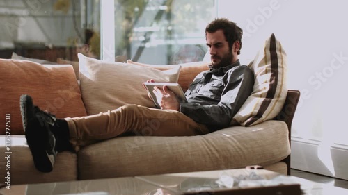 Man relaxing on a beige couch reading a book with a calm mood in a modern living room.