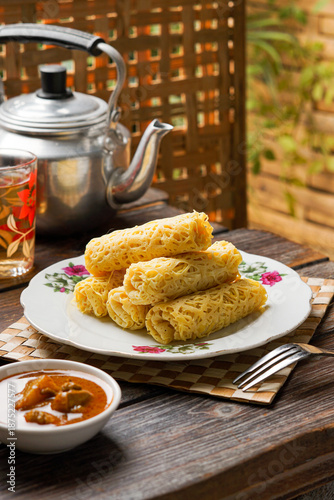 Roti Jala served with rich curry sauce is a traditional Malay dish made from delicate net crepes paired with flavorful spiced curry commonly enjoyed for breakfast festive meals and special occasions.
