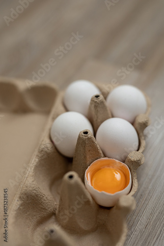 Vertical closeup of egg carton, one egg is broken