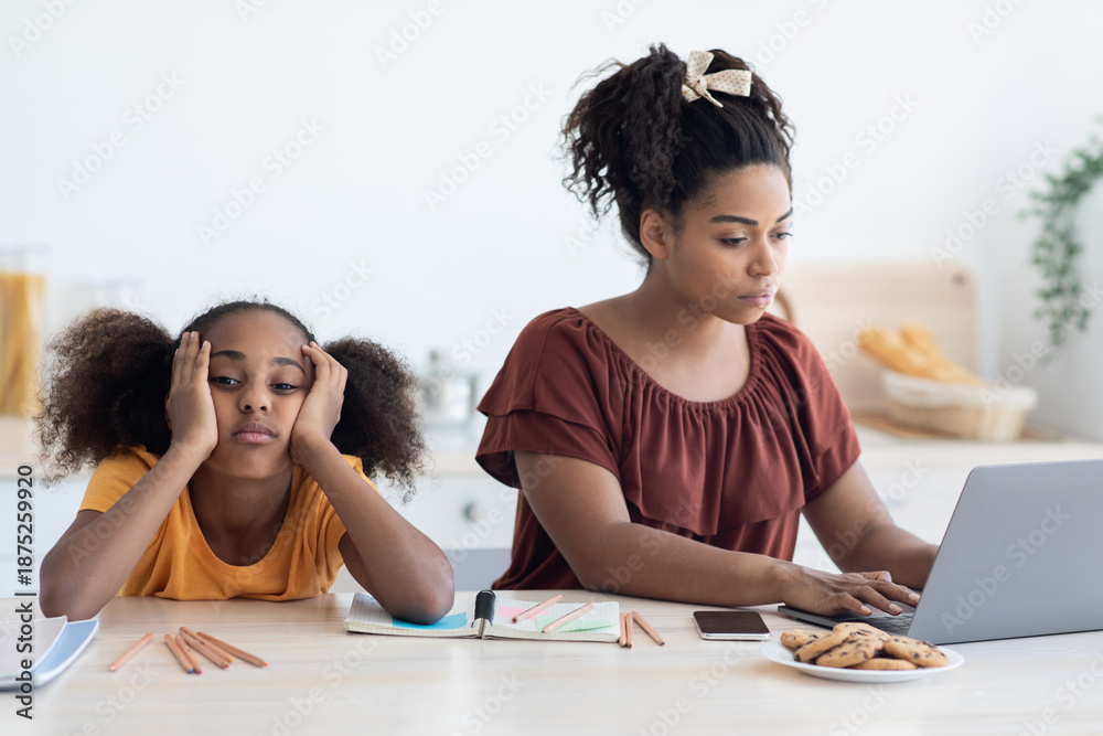 Obraz premium Black woman freelancer typing on laptop, working from home, bored daughter sitting by her, leaning on her hands, single mother does not paying attention to her kid teen girl, kitchen interior