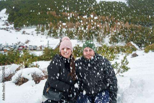 Young couple enjoying winter snowfall in mountain forest
