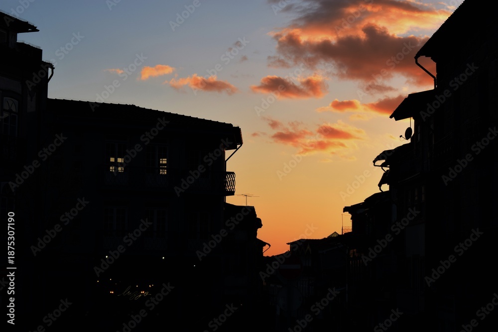Obraz premium Silhouette of old city buildings against sunset sky with sparse clouds
