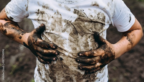 Child's hands covered in mud, playing in the dirt outdoors with a dirty t-shirt