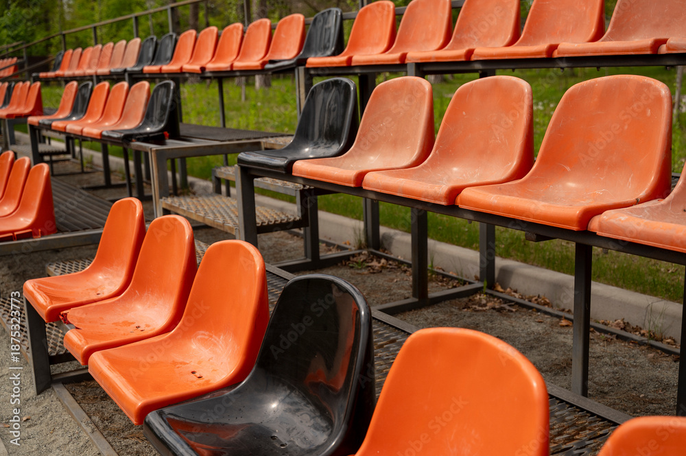 Naklejka premium Close up of Rows of empty orange and black plastic seats on grandstand near outdoor sports stadium
