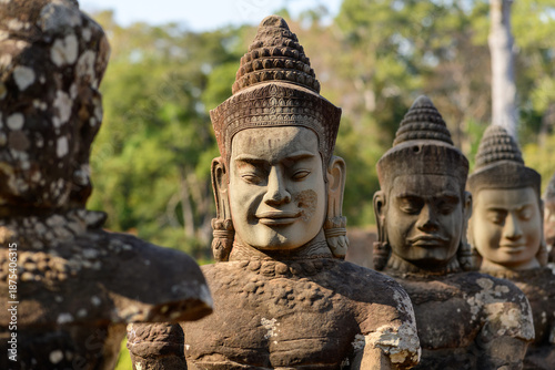 Detailed view of ancient stone guardian figures lining the entrance bridge of Angkor Thom near Siem Reap, Cambodia. The expressive Khmer sculptures are illuminated by warm daylight, with textured