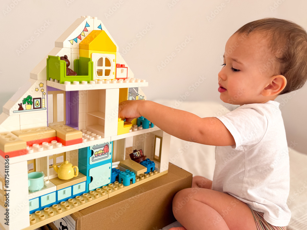 Fototapeta premium Toddler playing with a colorful lego duplo dollhouse