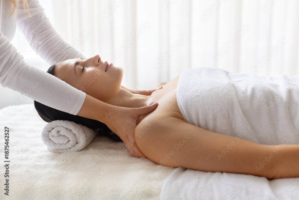 Obraz premium Young beautiful woman relaxing during professional spa neck and shoulder massage, lying on treatment bed, calm wellness atmosphere focused on beauty care, selfcare, and relaxation