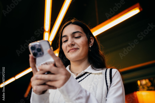 фотографія Woman smiling while reading something on smartphone screen, emphasizing satisfaction and ease of digital interaction in modern tech culture