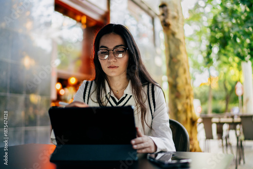 Foto Woman using smartphone while holding tablet under arm, paused mid‑motion to engage mobile screen, highlighting integrated digital device usage in everyday tech life