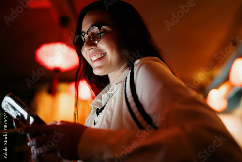 Фотография Close‑up of a smartphone screen glow reflecting on the user’s face, while she holds a stylus and interacts with content, capturing immersive mobile technology use