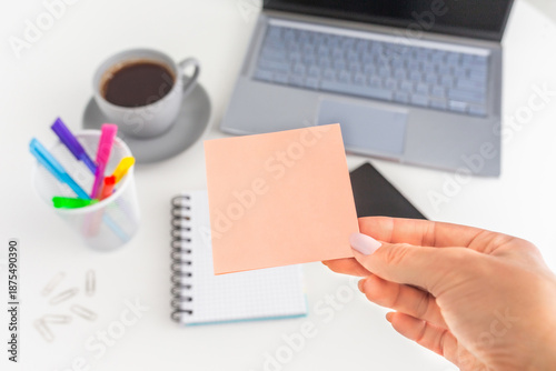 Woman's hand holding a blank pink sticky note over office desk (Copy space). 