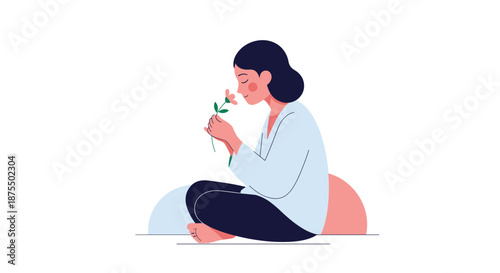 Calm and serene woman sitting cross-legged on the floor, peacefully smelling a delicate pink flower with her eyes closed.