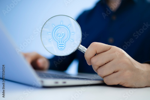 Businessman using laptop holding magnifying glass with lightbulb icon for ideas and innovation, Problem Solving Concept