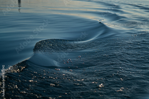 Water waves ripple, reflecting sunlight in a close-up shot from a moving vessel