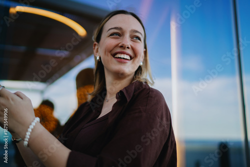 Vászonkép Joyful woman smiling while holding smartphone, enjoying mobile interaction, symbolizing cheerful lifestyle, positive online communication and modern digital self-expression