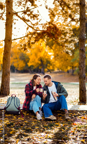 Tableau sur toile Romantic young multiracial couple enjoying a date in an autumn park, sitting on grass drinking tea