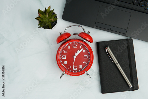 Фотография Top view office workspace with red alarm clock, notebook, pen, laptop, and plant