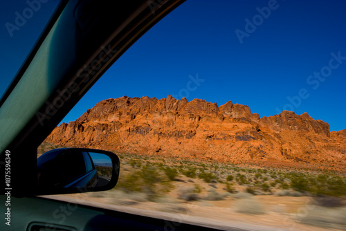 The driver's view of a side mirror, and the open window, a road trip through Red Rock Canyon.