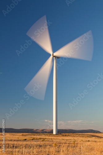 Single wind turbine spins in an open Oregon field beneath a clear blue sky, representing renewable energy and sustainability.