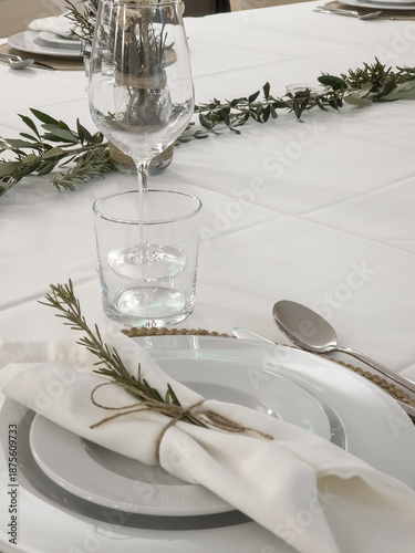 Obraz na plátně Elegant banquet table set with white plates, linen napkin tied with twine and rosemary, glassware and green foliage centerpiece prepared for a formal celebration dinner reception