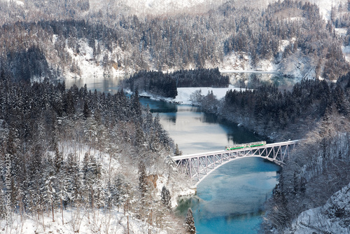 Wallpaper Mural A local train of JR Tadami railway line traveling through the snowy mountainside onto a bridge over the peaceful water of Tadami River on a sunny winter day in Mishima Town, Oku-Aizu, Fukushima, Japan Torontodigital.ca