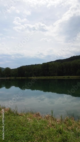 Peaceful lake reflection at Lac du Bouloc, France, with green forest and mountains.
