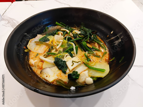 Spicy mala soup served in a black bowl, filled with vegetables and herbs, rich chili broth, hot flavor, Asian comfort food style.